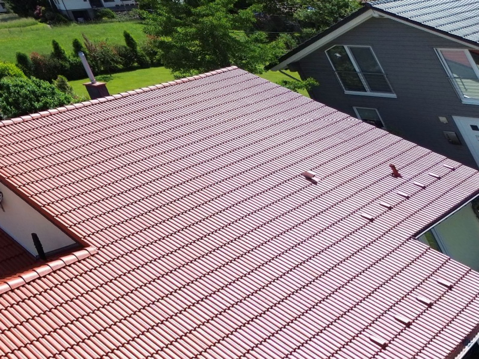 Luftaufnahme desselben Daches nach der Beschichtung: frisch leuchtend rotes Ziegeldach.