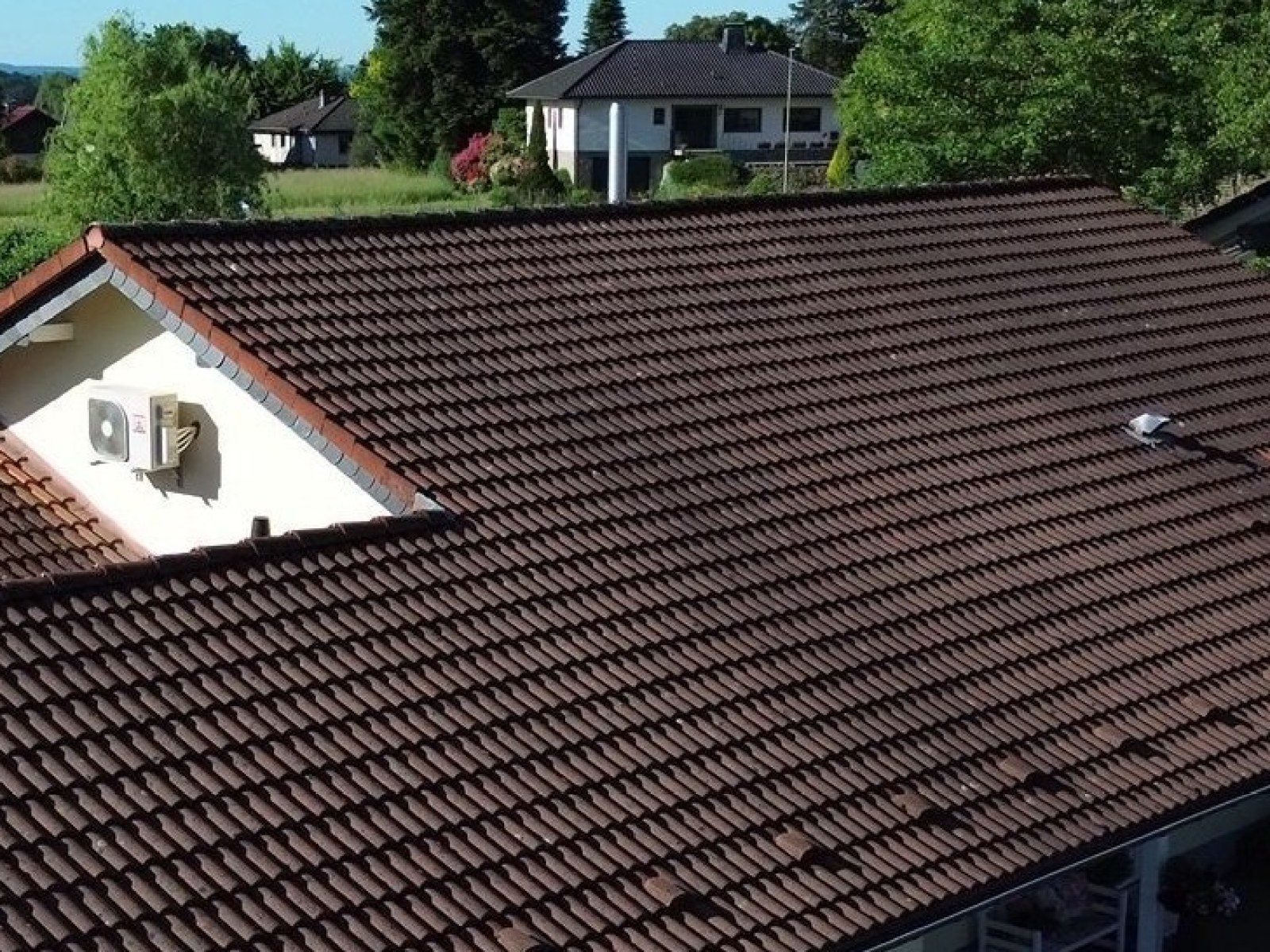 Luftaufnahme eines Winkelbungalows vor der Bearbeitung: dunkelbraunes, verwittertes Ziegeldach.