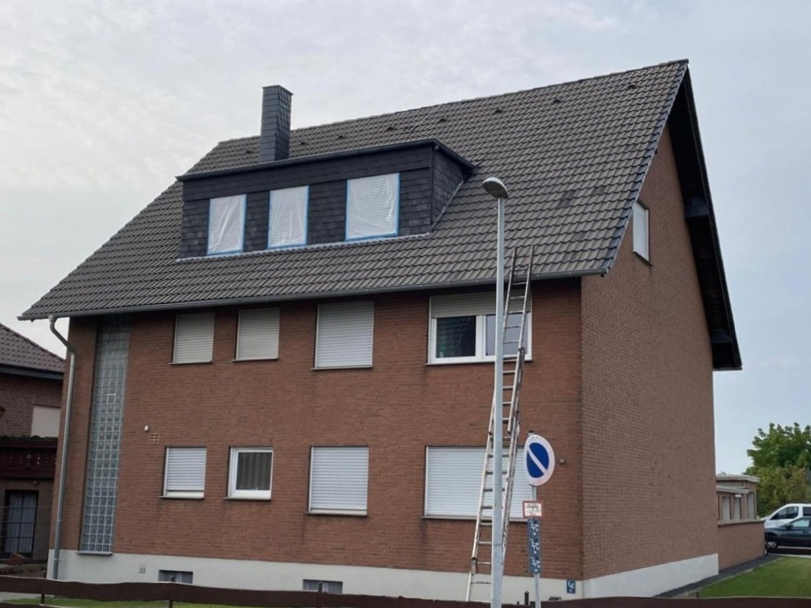 Steildach mit Gaube vor der Bearbeitung: verwittertes, fleckiges dunkles Ziegeldach, Leiter am Haus angestellt.