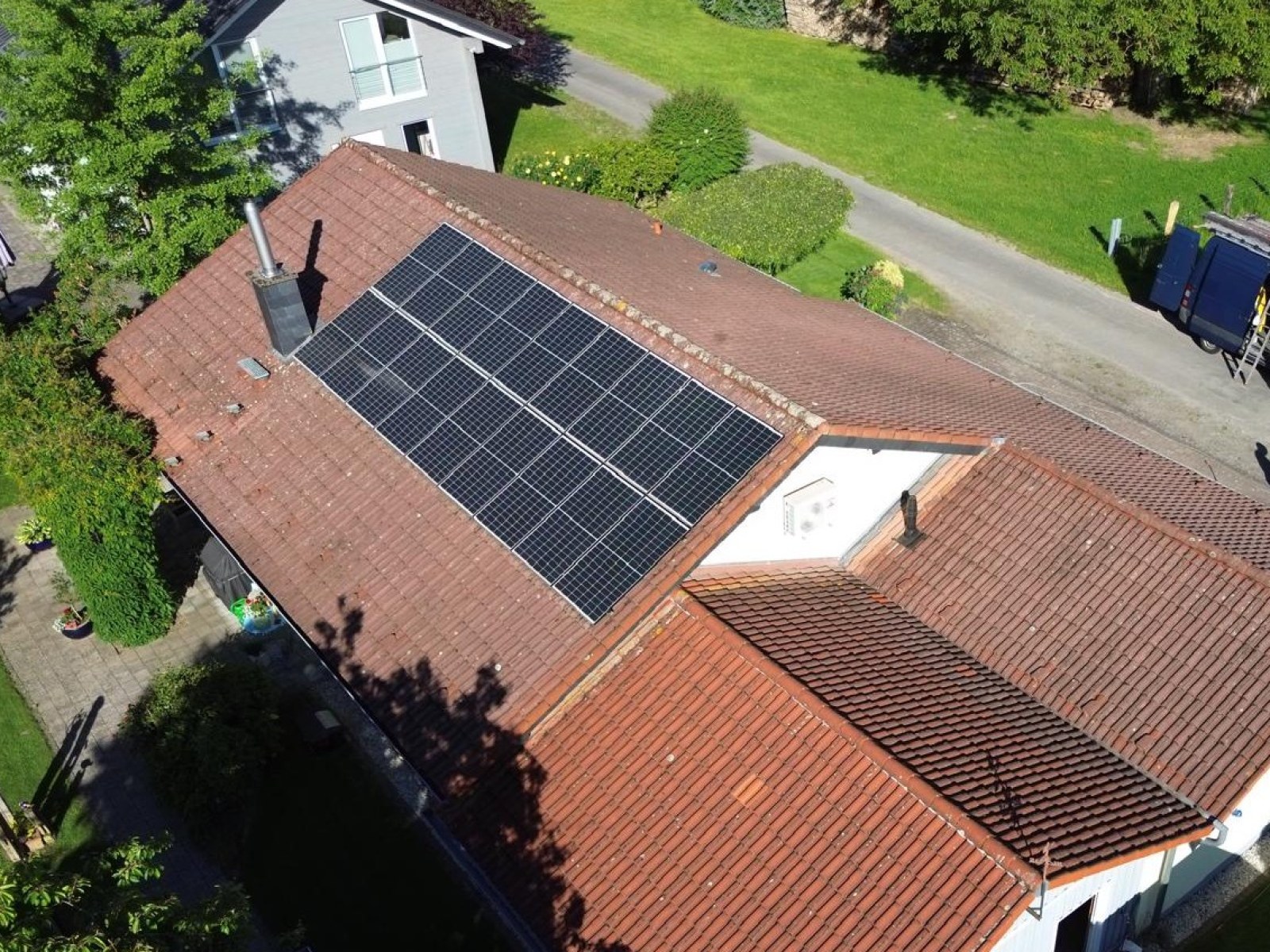 Luftaufnahme eines Landhauses mit Solarmodulen vor der Bearbeitung: stark verwittertes, fleckiges rotbraunes Ziegeldach.